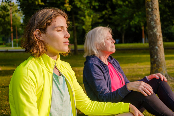 Portrait of grandmother and granddaughter meditating together in the park at sunset. - Photo, Image