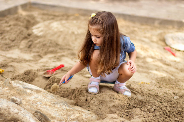 Schattig klein meisje graven zand te vinden botten in de zandbak - Foto, afbeelding
