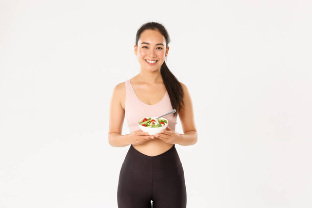 Sport, jólét és aktív életmód koncepció. Portré boldog ázsiai női sportoló, fitness lány mosolyog, miközben eszik az egészséges saláta, vigyáz, vagy testsúly diéta, testmozgás, hogy tökéletes test - Fotó, kép