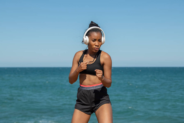 Афроамериканка в наушниках занимается боксом на открытом воздухе - Фото, изображение