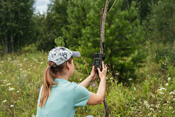 Young woman scientist biologist zoologist sets camera trap for observing wild animals in summer taiga forest to collect scientific data Environmental protection, monitoring of rare and endangered animal species, ecology World Wildlife Day - Photo, Image