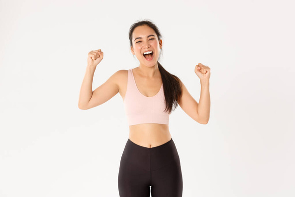 Sport, wellbeing and active lifestyle concept. Empowered and strong asian female athlete, fitness girl encourage herself for good workout, fist pump and shouting supportive, gaining goal - Photo, Image