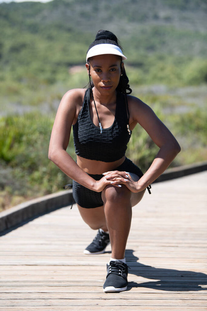 Femme afro-américaine concentrée s'étirant en regardant la caméra : concept de course et d'exercice. - Photo, image
