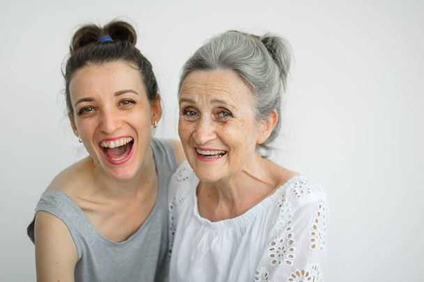 Щаслива старша мати обіймає свою дорослу дочку, жінки сміються разом, щира сім'я різних вікових поколінь веселиться на білому тлі, день матері
. - Фото, зображення