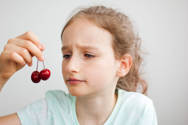 Yllättynyt tyttö pitelee kirsikoita kädessään. Terveellinen syöminen käsite, terveellisiä makeisia - Valokuva, kuva