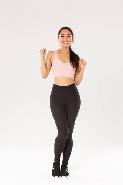 Sport, gym and healthy body concept. Full length of encouraged and motivated asian brunette girl ready for fitness training, fist pump and shouting in rejoice, gain goal with workout training app - Foto, immagini