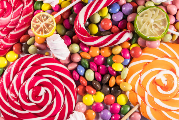 Background of colorful chocolate candies, lollipops, candy cane and marshmallows - Фото, изображение