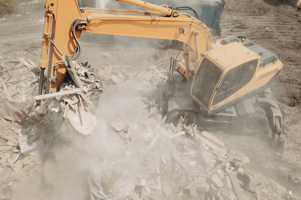 Koparka rozbija budynek i ładuje odpady budowlane do ciężarówki z wiadrem. Rozbiórka budynku - Zdjęcie, obraz
