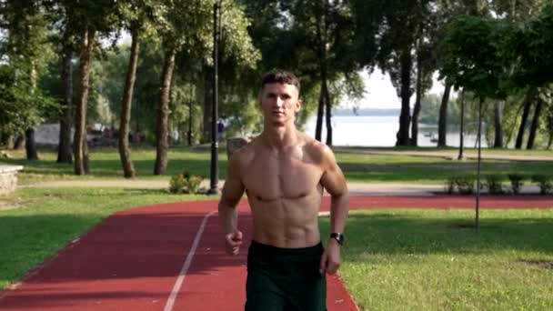 sportieve man met gespierd lichaam loopt op de renbaan in het park, sportief - Video
