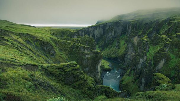 Epic aerial view of Fjadrargljufur Canyon in southern Iceland. A green lush canyon with steep rocks carved into picturesque landscape in moody hazy atmosphere. - Фото, зображення