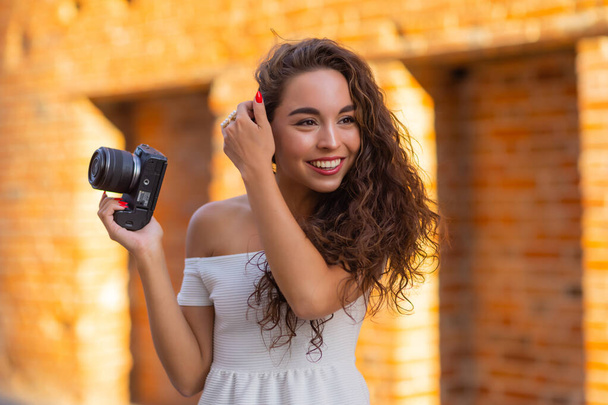 Young attractive female student or tourist using a mirrorless camera while walking in summer city. Woman takes pictures and enjoy weather. - Foto, Imagem