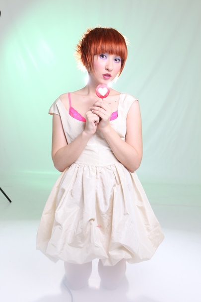 Girl with lollipop heart in white dress in studio - Fotoğraf, Görsel