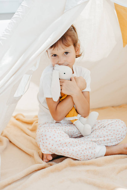 cute girl playing in teepee with fabric tilda bunny at home - 写真・画像