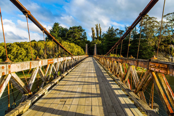 Picturesque wooden suspension bridge over a quiet river. South Island, New Zealand. Incredible cloudy sunset. Southern Scenic Route. The concept of eco and photo tourism  - Photo, image