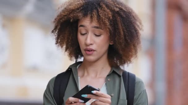 Зручний портрет втомленої молодої афроамериканської дівчини, яка загубилася у великому місті, не може знайти будівлю, яку вона шукає. Тисячолітній студент змішаної раси використовує мобільний додаток на смартфонах маршруту - Кадри, відео
