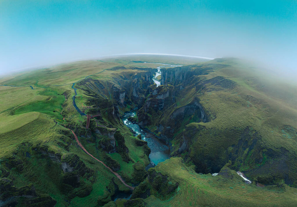 Epische Luftaufnahme des Fjardrgljfur Canyon im Süden Islands. Eine grüne, üppige Schlucht mit steilen Felsen, die in eine malerische Landschaft in stimmungsvoller nebliger Atmosphäre gemeißelt sind. - Foto, Bild