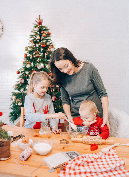 mamá e hijas cocinando pan de jengibre de Navidad en una habitación con un tre de Navidad - Foto, imagen