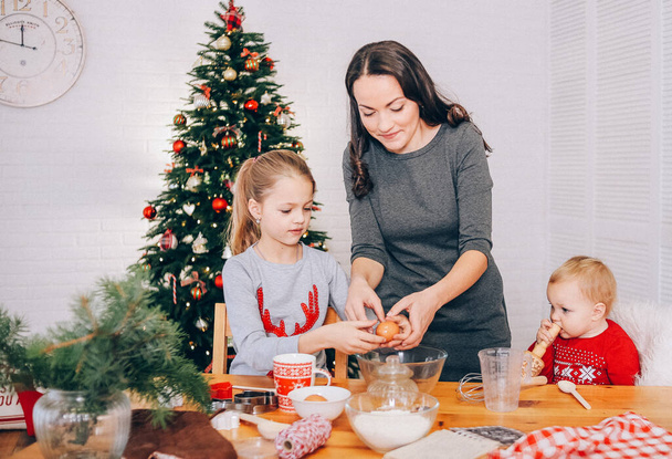 mom and daughters cooking christmas gingerbread in a room with a christmas tre - Foto, Imagen
