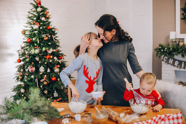 mom and daughters cooking christmas gingerbread in a room with a christmas tre - Photo, Image