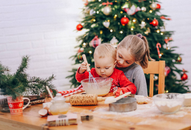 two girls prepare dough for Christmas cookies on the background of a Christmas tre - Foto, Bild