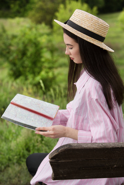 Молода красива дівчина читає книгу, сидячи на дерев'яній лавці в парку
. - Фото, зображення