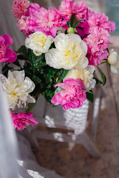 un bouquet di peonie fresche bianche e rosa in un vaso di vetro trasparente con belle ombre vicino a una tenda di tulle bianco, in sfocatura - Foto, immagini