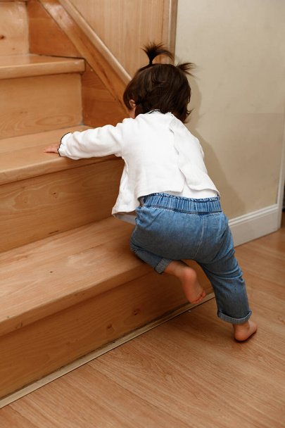 Boso maluch próbuje wspiąć się na drewniane schody na czworaka - Zdjęcie, obraz