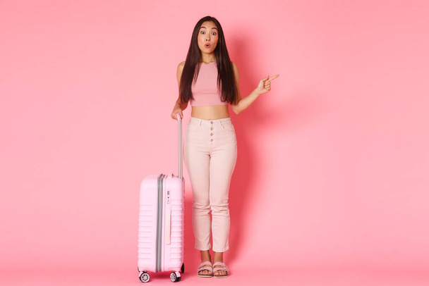 Podróże, wakacje i koncepcja wakacje. Pełna długość imponujący i ciekawy atrakcyjny azjatycki dziewczyna turysta w letni strój zwiedzanie zwiedzanie, wskazując w prawo i wyglądają zastanawiające, trzymając walizkę - Zdjęcie, obraz