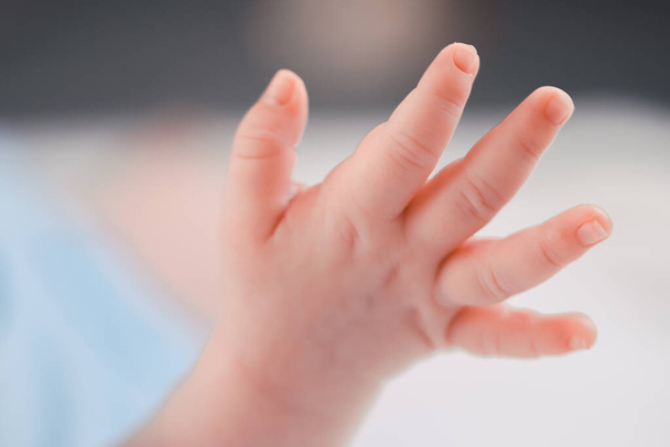 Raised hand of newborn Caucasian baby sleeping on bed with open fingers in the middle with blurred background, very close-up side view. Close up of motherhood, health and childcare concept. - Φωτογραφία, εικόνα