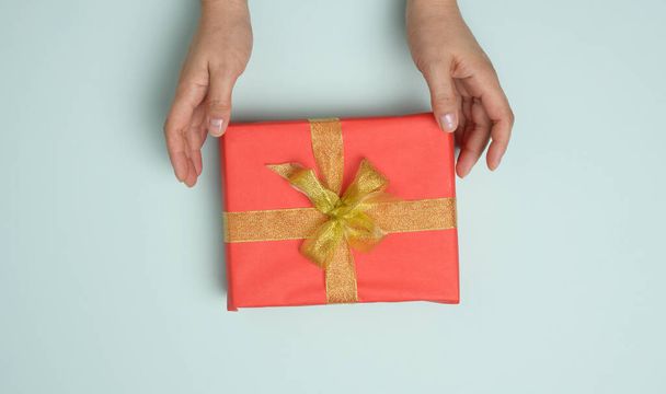 mains féminines tiennent boîte cadeau rouge sur un fond bleu, concept de félicitations pour l'anniversaire, vue de dessus - Photo, image