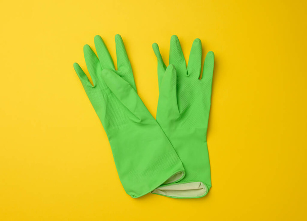 黄色の背景にクリーニングのための緑の保護ゴム手袋のペア、トップビュー - 写真・画像