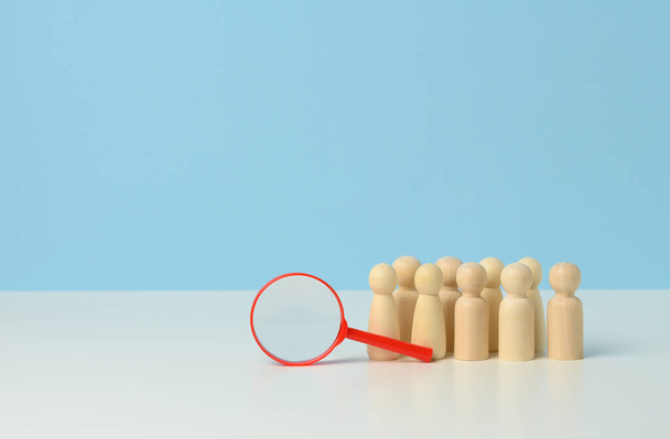 wooden figures of men on a blue background and a red magnifying glass. Recruitment concept - Photo, Image