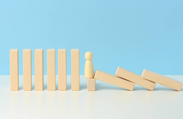 figures of men restrain the falling of wooden blocks, the effect of dominoes on a blue background. concept of teamwork, ability to prevent the consequences of the influence of external sources - Foto, Bild
