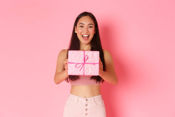 休日、お祝いやライフスタイルの概念。ギフトを作る陽気な美しいアジアの女の子のウエストアップ,ラップボックスに友人の誕生日プレゼントを与えます,ピンクの背景に立って,お祝い - 写真・画像