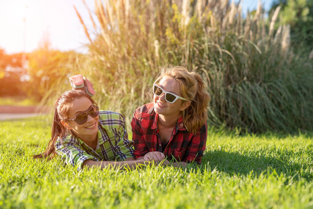 two young pretty teenager girls best friends laying on grass at sunny summer day. - Zdjęcie, obraz