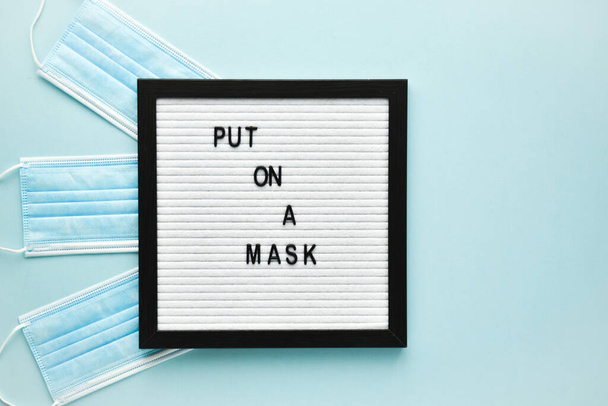 A medical mask and a text message on a felt board are applied to the mask on a light blue background. Poster, banner virus protection. An empty space. - Photo, image