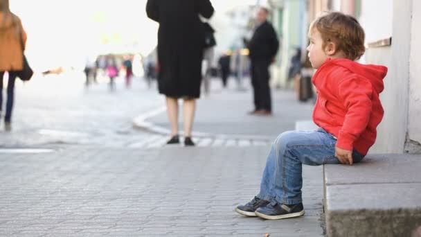 mały chłopiec siedzi sama na ulicy - Materiał filmowy, wideo