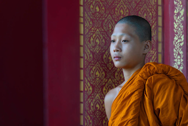 buddhist novice monk in orange robe standing by window in buddist temple - Foto, immagini