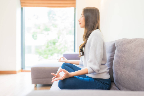 Porträt schöne junge asiatische Frau Meditation auf Sofa im Wohnzimmer Interieur - Foto, Bild