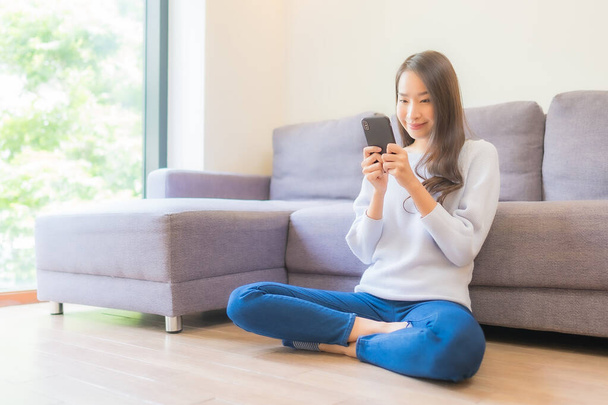 Ritratto bella giovane donna asiatica uso smart cellulare sul divano in salotto interno - Foto, immagini
