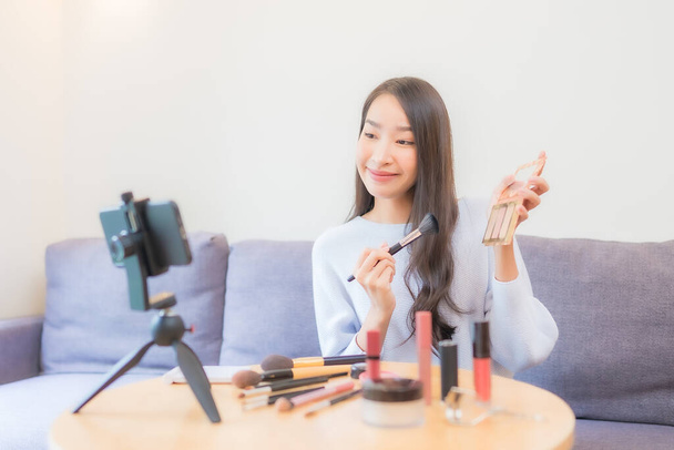 Portret mooie jonge aziatische vrouw beoordeling cosmetische make-up online thuis - Foto, afbeelding