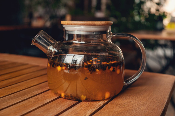 Tea with sea buckthorn in glass teapot in cafe. Herbal tea to strengthen the immune system - Фото, зображення