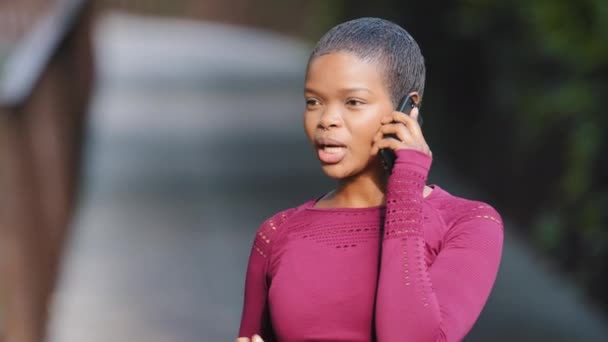 Headshot πορτρέτο 25s Αφρικής μαύρο κορίτσι σε αθλητικά ρούχα στέκεται υπαίθρια συζήτηση στο smartphone κατά τη διάρκεια της πρωινής άσκησης στο πάρκο. Νεαρή γυναίκα δρομέας έχει ευχάριστη συνομιλία από το τηλέφωνο, γέλιο, αισθάνεται χαρούμενος - Πλάνα, βίντεο