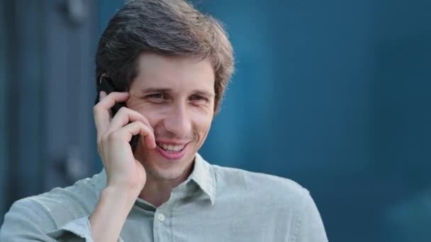 Talking on phone. Confident positive male freelancer holding cellphone at his ear giving professional consultation to customer. Young man discuss business with friend or make order of service goods - Footage, Video