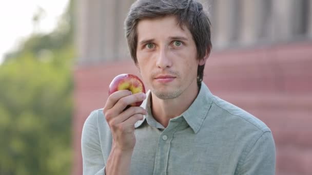 Молодой привлекательный веселый мужчина держит яблоко в руке, нюхает спелые фрукты, обнаруживает отсутствие запаха, ничего не чувствует. Белый парень, напуганный обонянием исчезновения, симптомы коронавирусной концепции - Кадры, видео