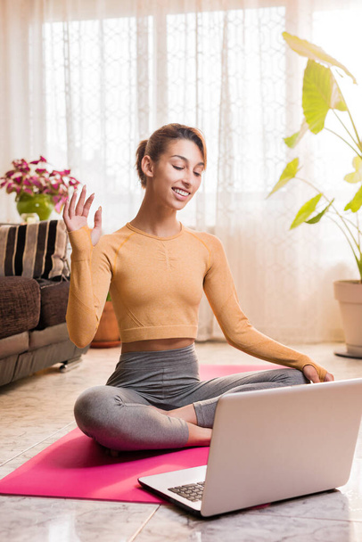 Személyi edző belépett laptoppal egy virtuális osztálytermi videokonferencián otthon a karantén alatt. Fiatal spanyol nő jóga óra - Fotó, kép