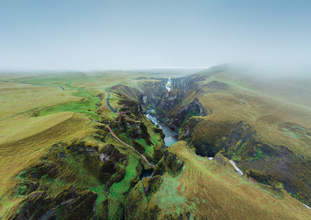 Επική εναέρια άποψη του φαραγγιού Fjadrarglujfur στη νότια Ισλανδία. Ένα καταπράσινο φαράγγι με απότομους βράχους χαραγμένους στο γραφικό τοπίο σε μελαγχολική θολή ατμόσφαιρα. - Φωτογραφία, εικόνα