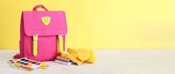 рюкзак и канцелярские принадлежности на столе на фоне цвета с местом для текста - Фото, изображение