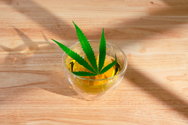 Um copo de chá de maconha quente na mesa de madeira. Cannabis chá de ervas com folha verde. - Foto, Imagem