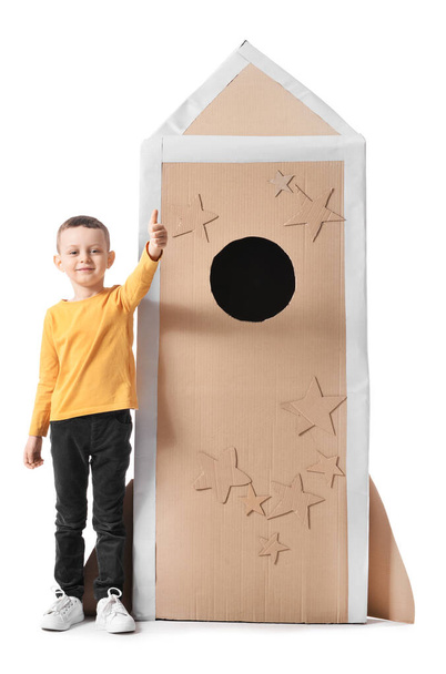 Schattig jongetje met kartonnen raket met duim omhoog op witte achtergrond - Foto, afbeelding